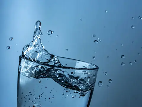 Water splashing in a clear glass against a blue background