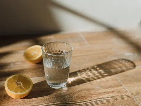 A glass of water beside lemon slices on a wooden table in sunlight