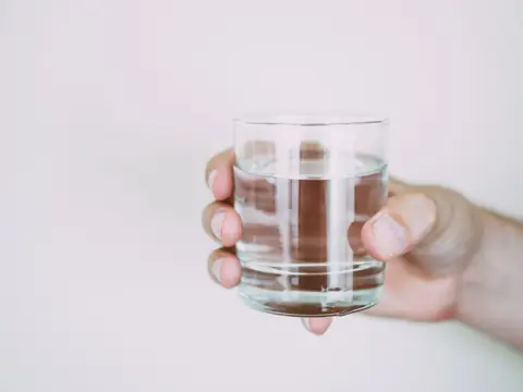 A hand holding a glass of water against a white wall