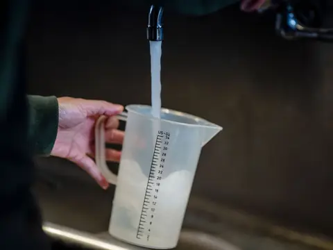 A measuring jug being filled under a running faucet
