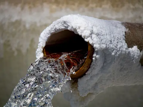 Water flowing from a pipe crusted with white mineral deposits