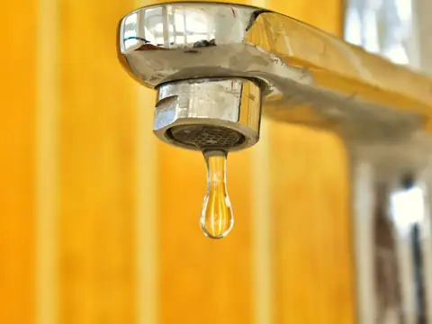 A drop of water hanging from a faucet spout
