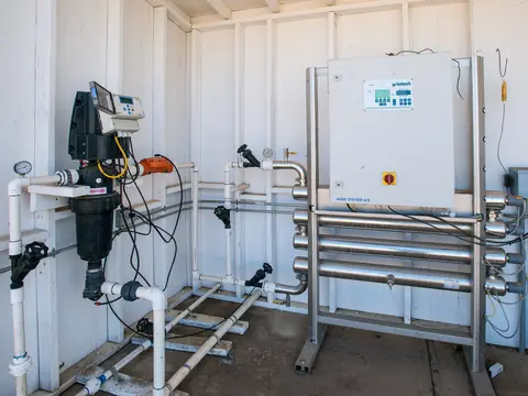 A water treatment room with a black filter housing, valves and stainless steel pipework