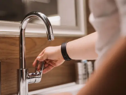 A hand turning the handle of a chrome faucet