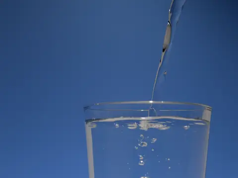 Water pouring into a clear glass against a blue background