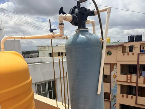A softener tank with its control valve plumbed into the water line outdoors in the sun
