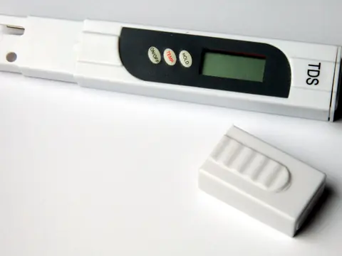 A handheld dissolved solids meter and its cap on a white surface