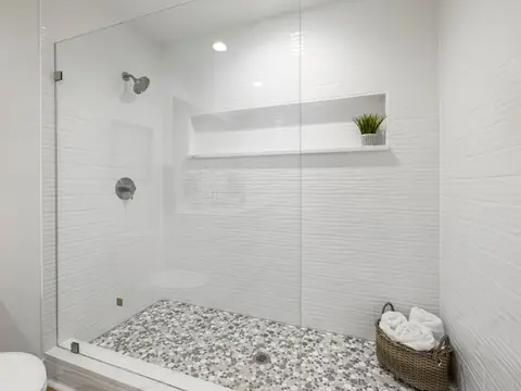 A clear glass shower panel in a white tiled bathroom