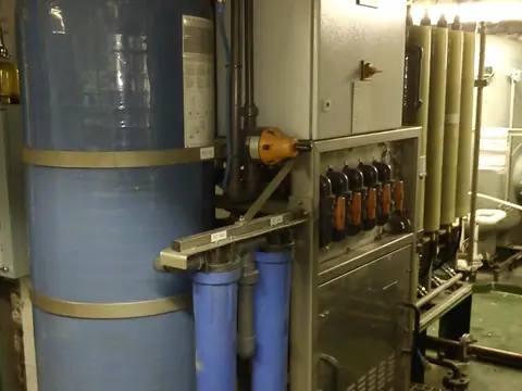 A tall pressure tank with blue filter housings beside it on a treatment rack